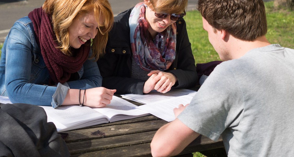 Studierende am Tisch, Gruppenfoto mit Heften auf Tisch