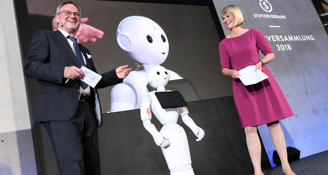 Podiumsfoto mit zwei Personen (Jürgen Handke und Gundula Gause) und humanoidem Roboter Yuki in der Mitte