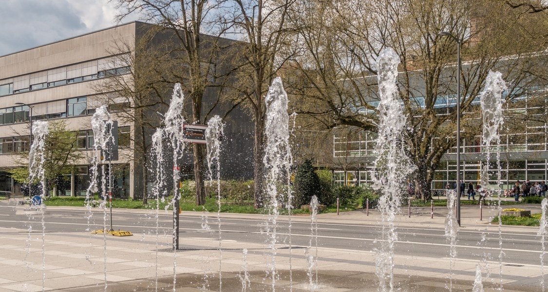 Wasserspiel - Wasserfontänen kommen aus Platz vor Erwin-Piscator-Haus, im Hintergrund Hörsaalgebäude