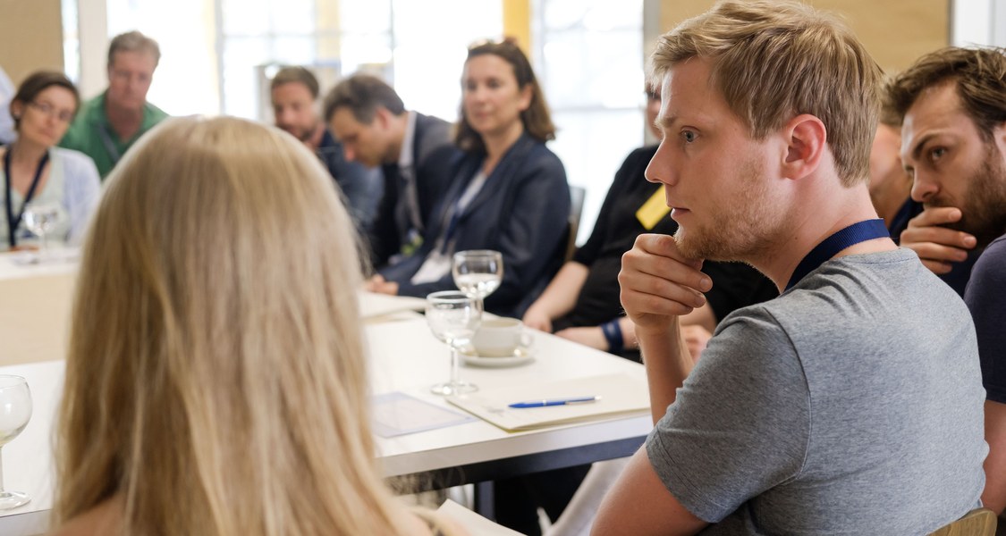 Gruppenfoto, Menschen sitzen um Tisch und sprechen miteinander