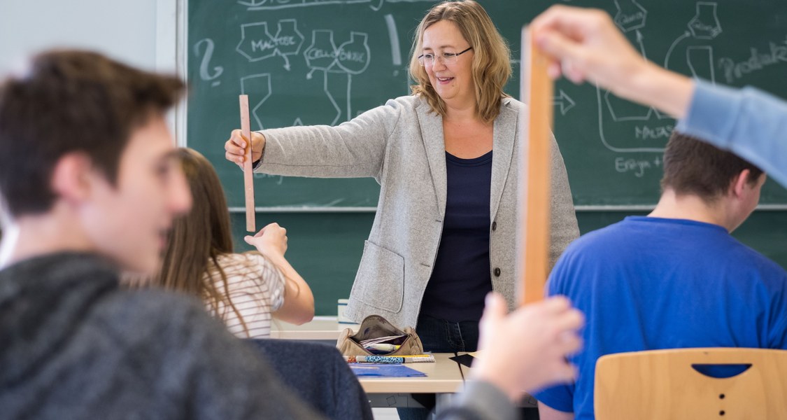 Lehrerin vor Tafel, Schüler von hinten, Lehrerin hält Lineal senkrecht