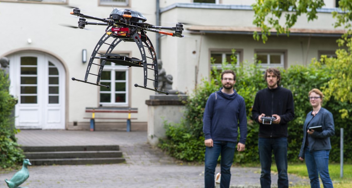 Studierende im Hintergrund, fliegende Drohne im Vordergrund