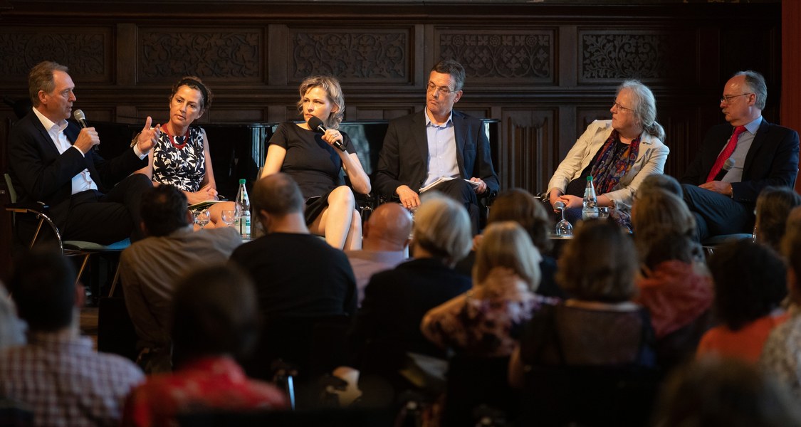 Gruppenbild der Podiumsdiskussion, im Vordergrund das Publikum