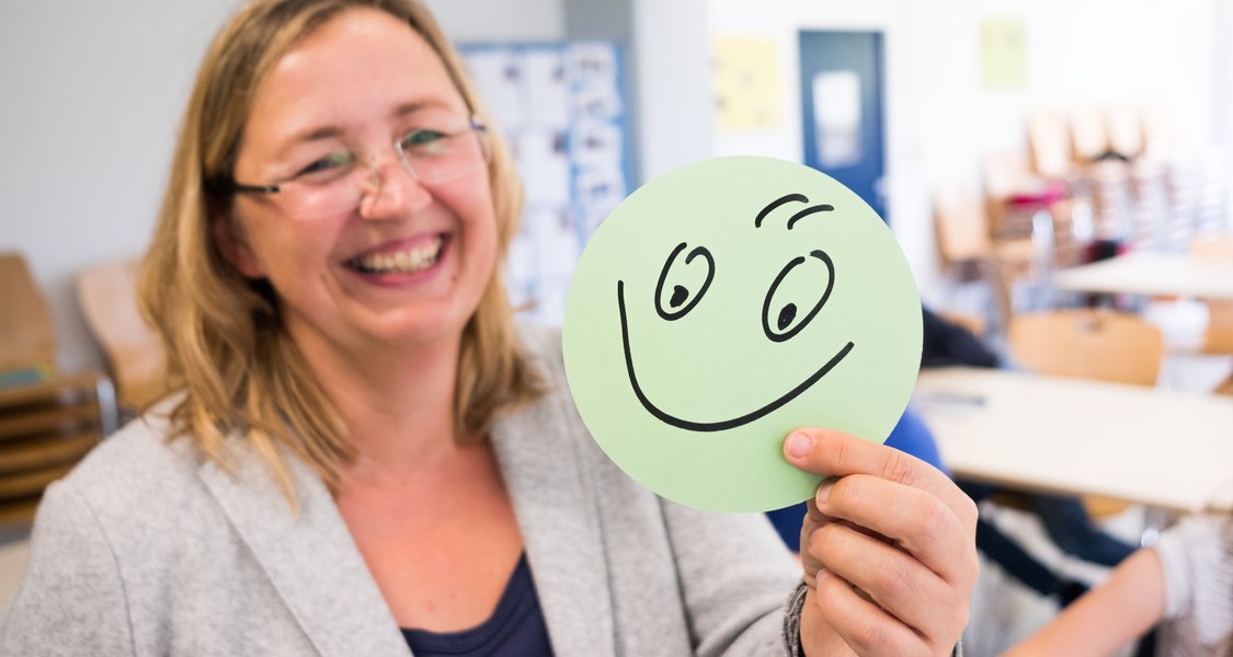 Frau hält runden Zettel mit Smiley in die Kamera