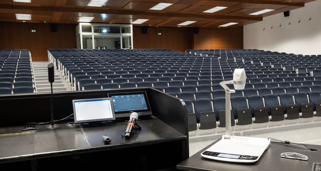 Blick vom Rednerpult im Audimax auf leere Stuhlreihen, im Vordergrund Mikrofon