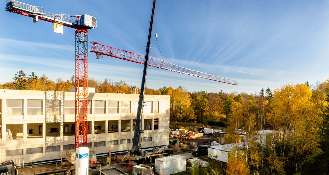 Blick auf Rohbau mit Baukran im Vordergrund. Ein Teil des Baukrans wird mit einem mobilen Kran abgebaut.