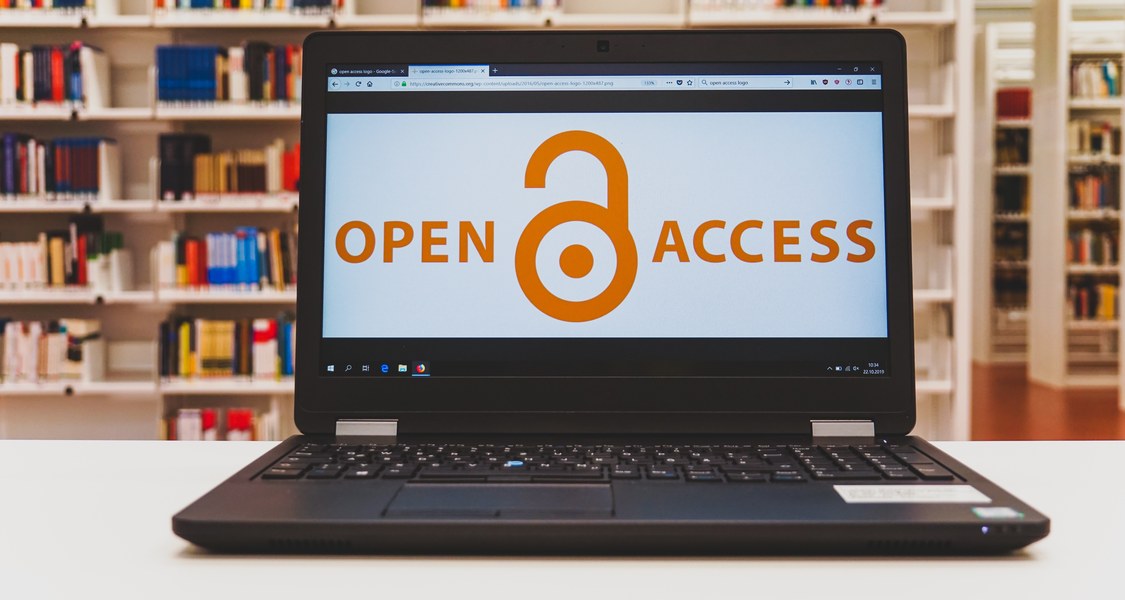 Notebook mit Schriftzug "open access" und einem Symbol eines offenen Vorhängeschlosses vor einer Bücherwand