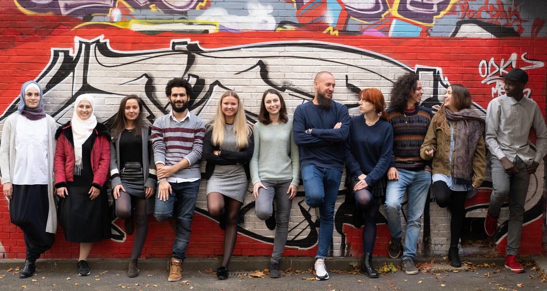 Studierende lehnen an einer Wand, die mit Graffiti besprüht ist.