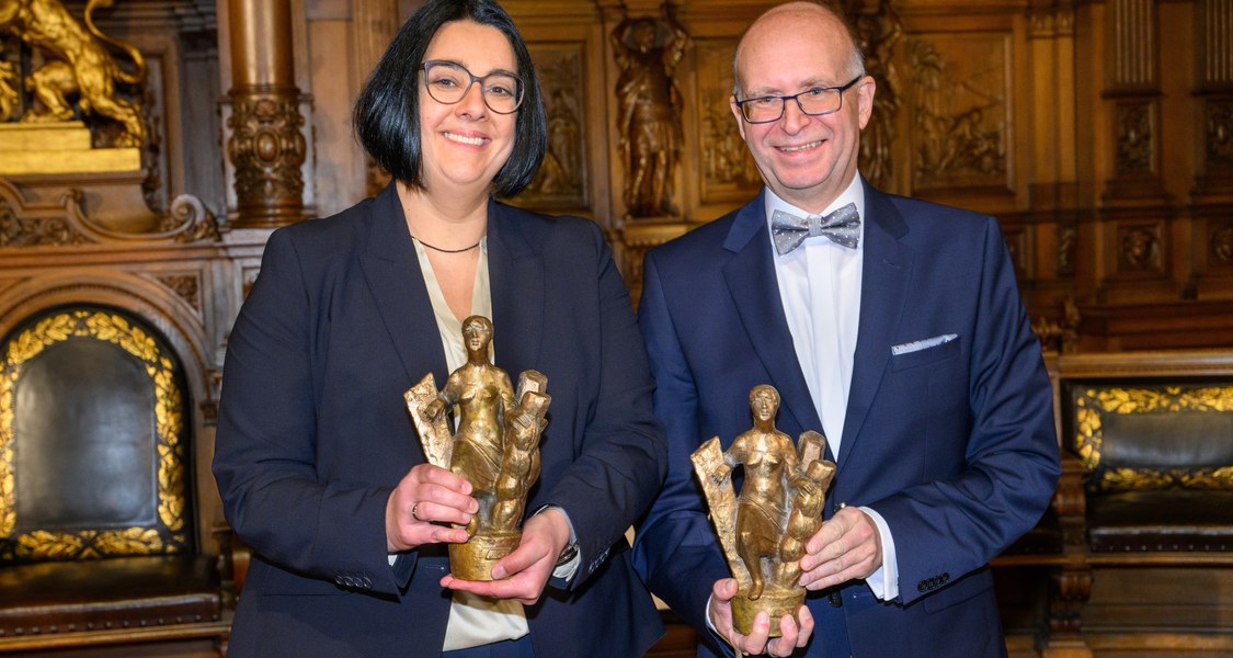 Die Preisträgerin und der Preisträger - beide halten eine kleine Skulptur in den Händen.