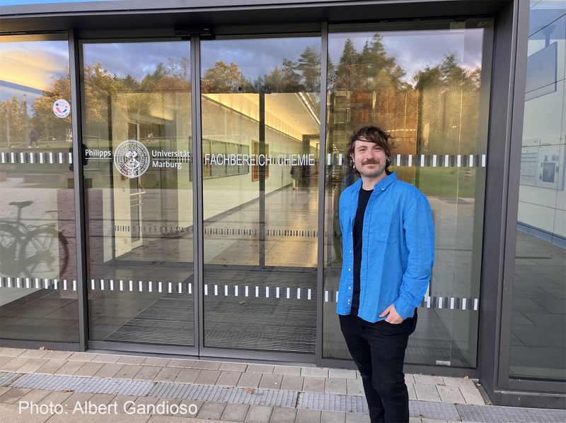 Junger Mann in blauem Jackett vor dem Eingang des Fachbereichs Chemie der Uni Marburg