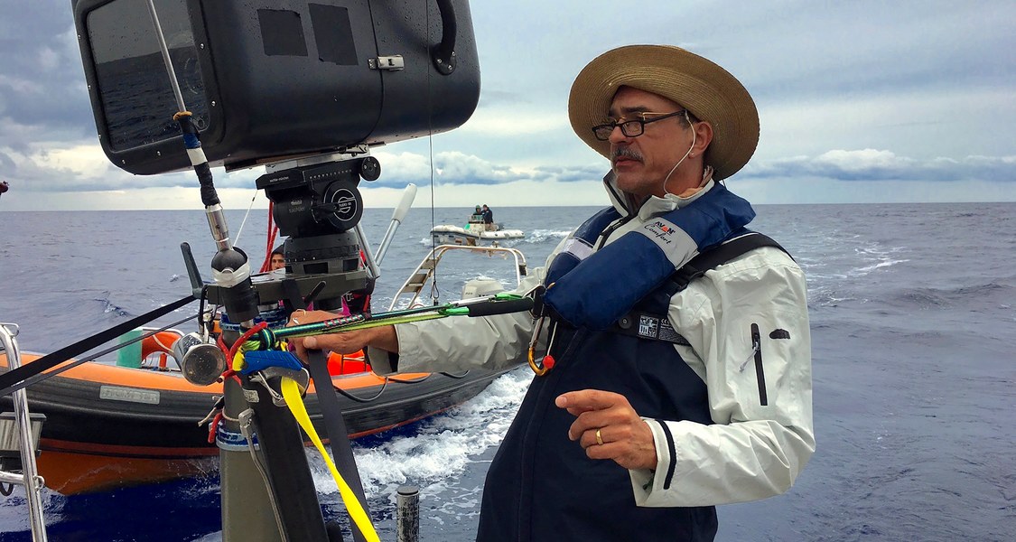 Benedict Neuenfels an Filmkamera, im Hintergrund Wasser mit einem Boot