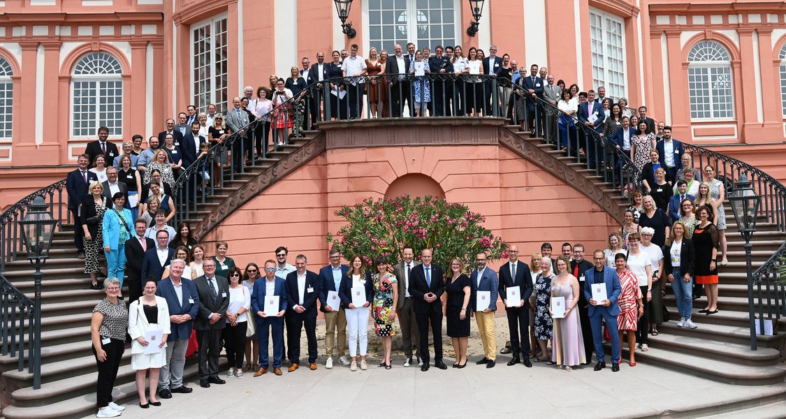 Gruppenfoto mit ca. 50-60 Personen, die auf einer repräsentativen geschwungenen Treppe von Schloss Biebrich in Wiesbaden stehen