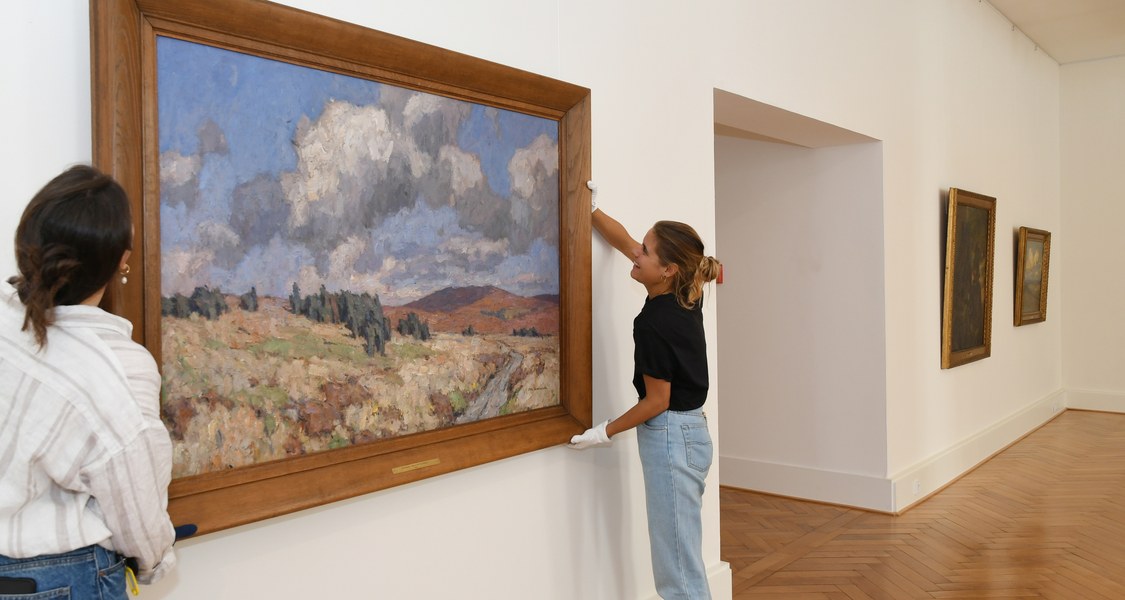 Zwei Mitarbeiterinnen des Museums hängen das Gemälde an die Wand