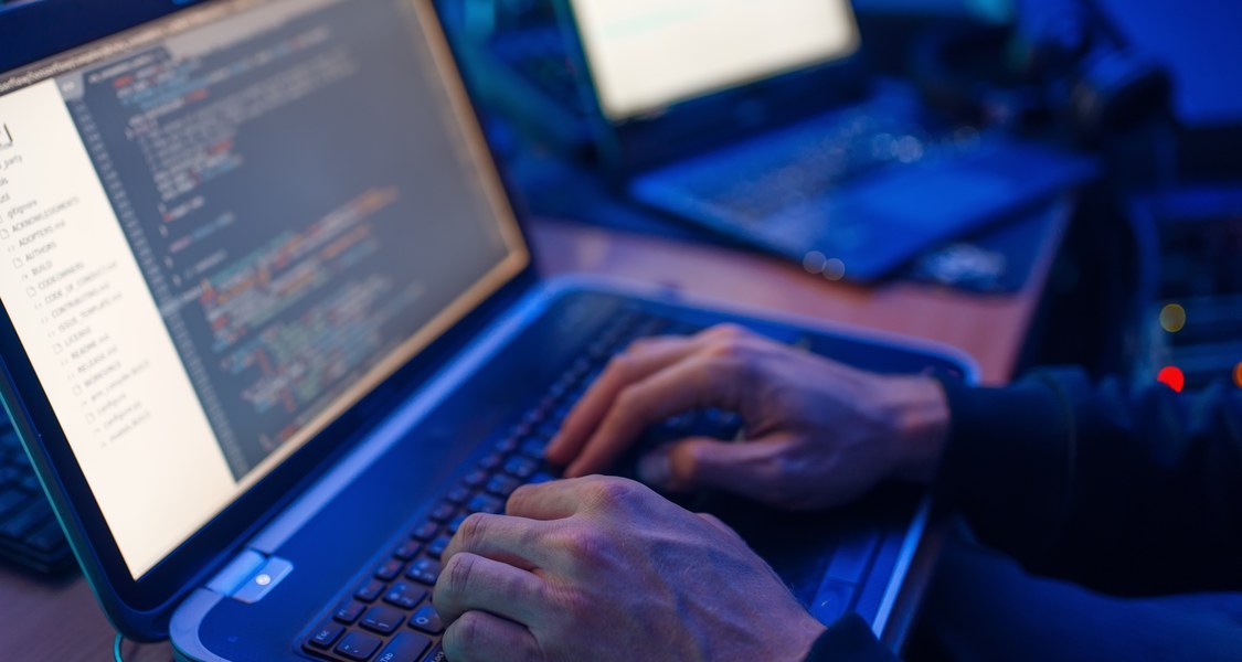 zwei Laptops mit Händen, im Hintergrund weitere Bildschirme