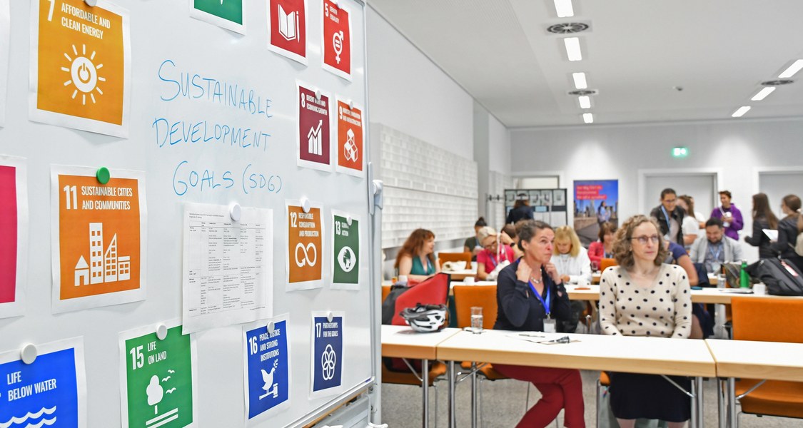 Teilnehmende der Lima Summer School 2023 in Marburg. Im Vordergrund ein Plakat mit bildlicher Darstellung der Nachaltigkeitsziele der Vereinten Nationen
