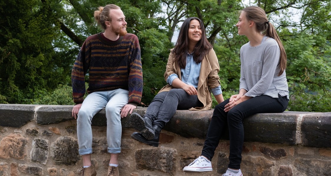 Gruppe von Studierenden im Gespräch, sitzend auf einer Mauer