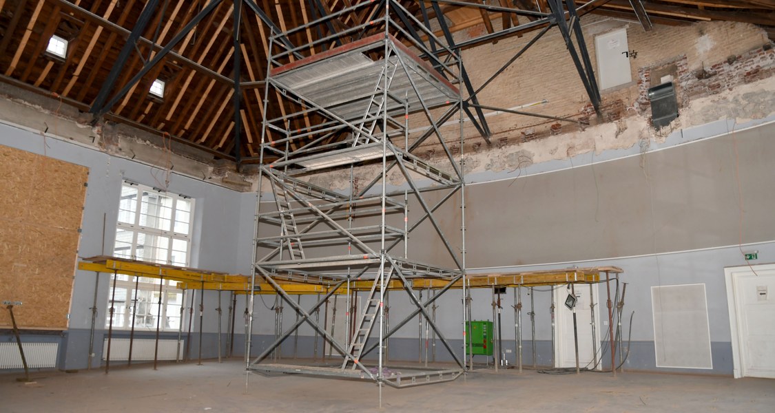 Panoramablick in den leeren Hörsaal, in dem noch in der Mitte ein Gerüst steht. Man kann von unten in den Dachstuhl sehen.