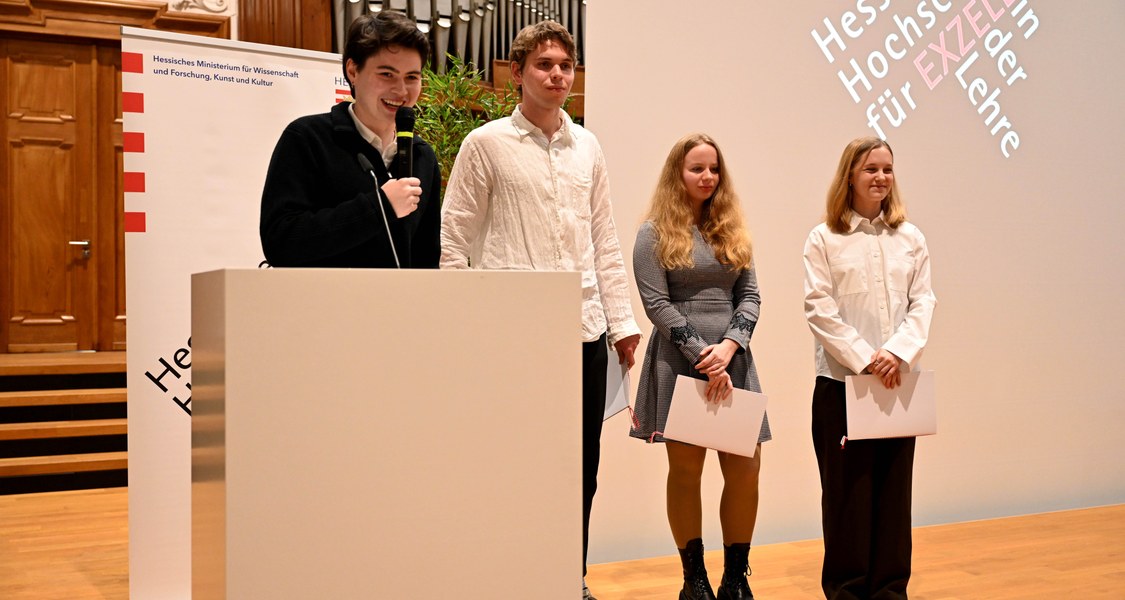 Vier Studierende am Rednerpult mit Urkunden in den Händen
