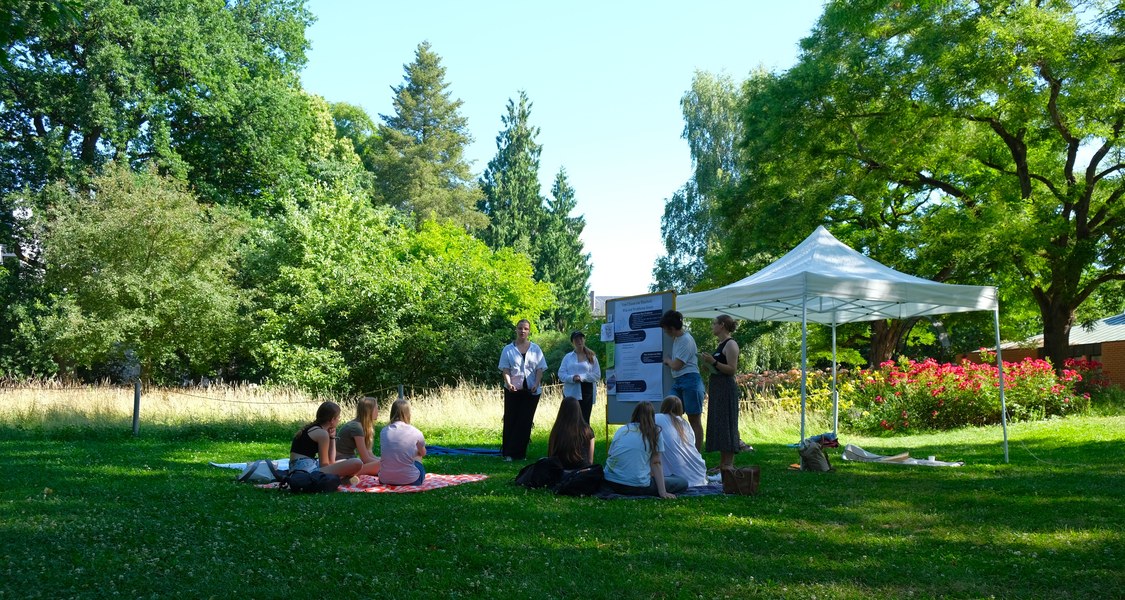 Sitzgruppe mit Studis und Schüler*innen mit Tableau und Zelt im Alten Botanischen Garten.