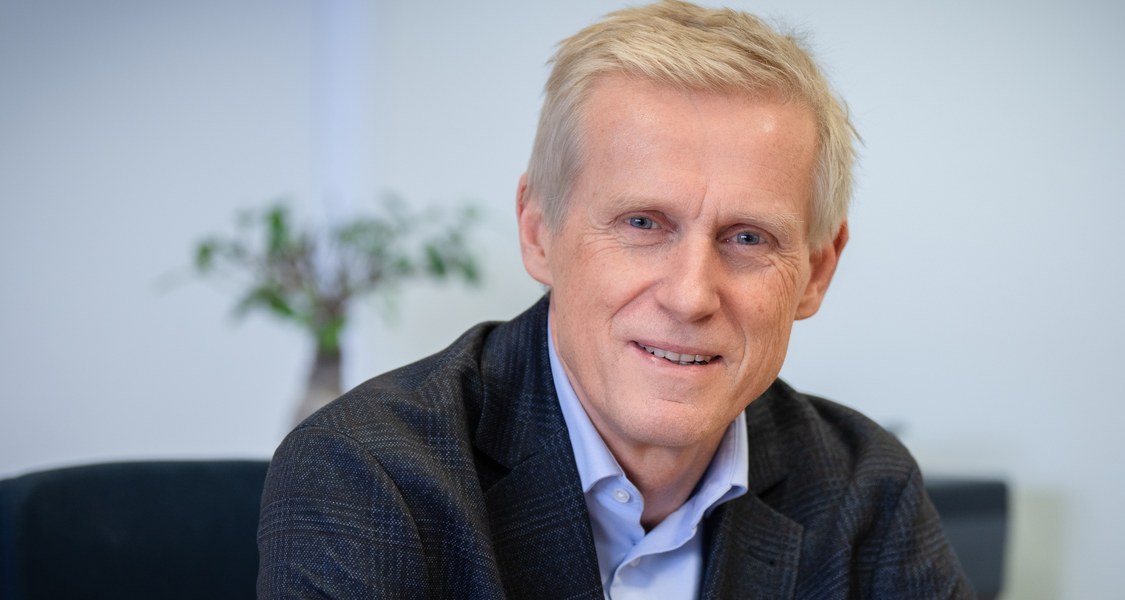 Mensch sitzt am Schreibtisch und schaut in die Kamera