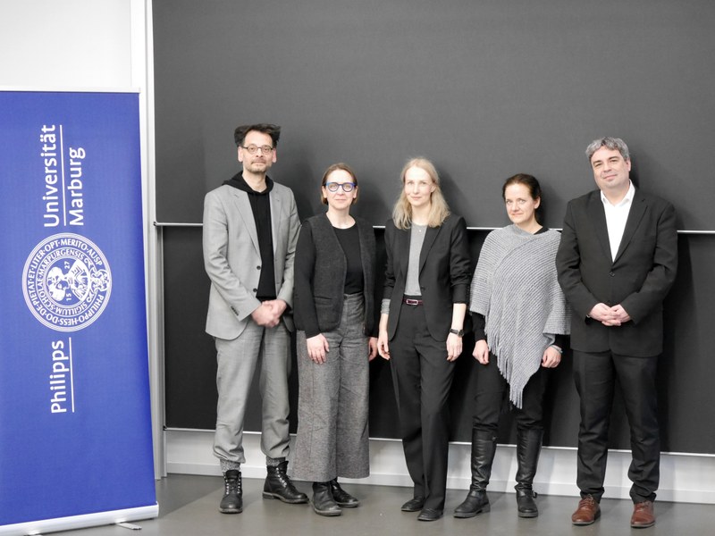 Gruppenbild, sechs Personen neben dem Logo der Universität Marburg