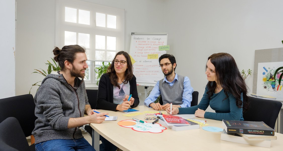 Studierende sitzen an einem Tisch und diskutieren