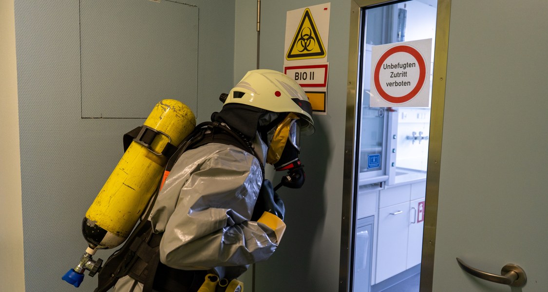 Person im Schutzanzug an einer Tür mit Warnhinweisen in einem Bio-Labor