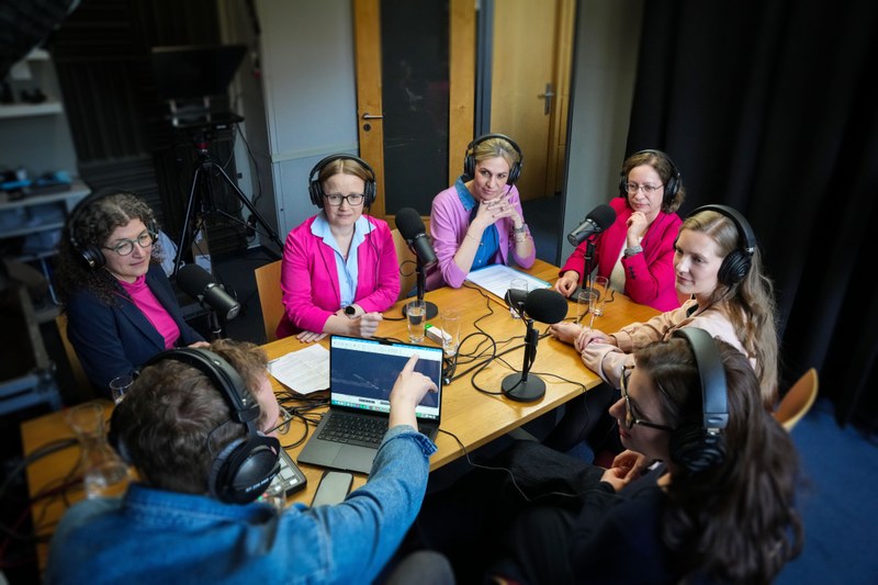 Gruppenfoto von fünf Personen mit Kopfhörern und Mikrofonen in einem Podcast-Studio
