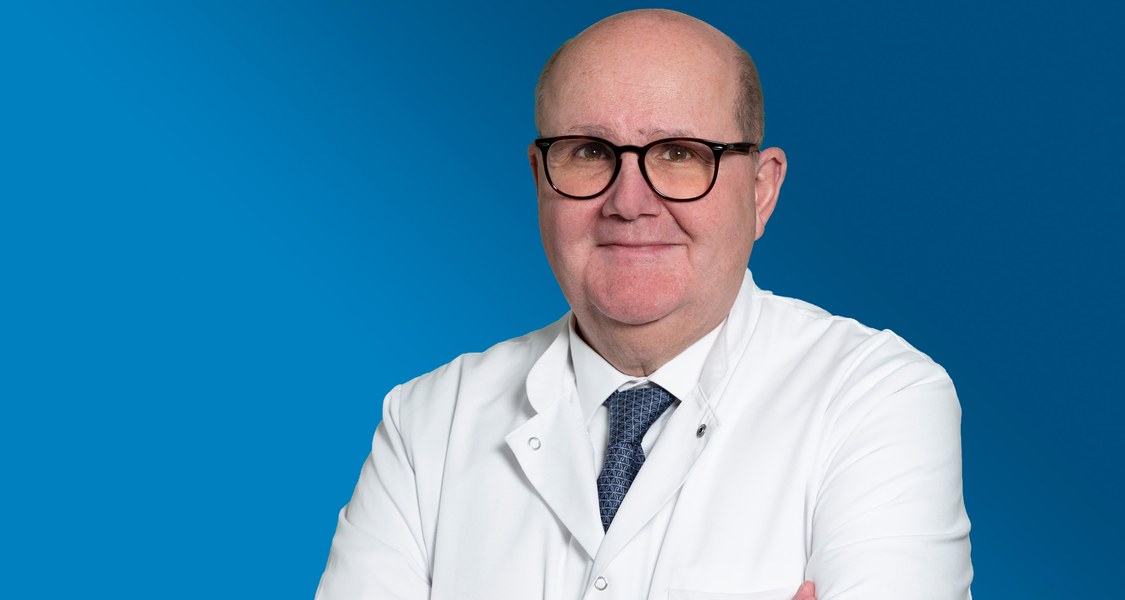 Porträtfoto Professor Bernhard Schieffer in Arztkittel vor blauem Hintergrund