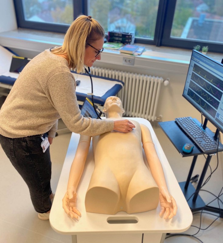 Ein Mensch tastet eine Simulationspuppe mit einem Stethoskop ab.