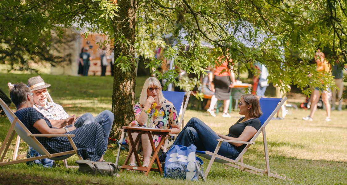 vier Personen sitzen auf Liegestühlen im Park.