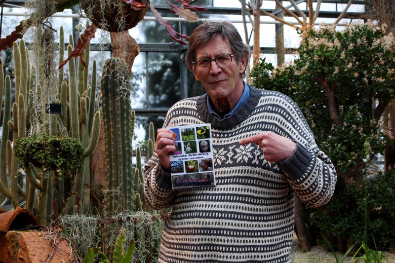 Das Foto zeigt Hartwig Bambey vom Sternbald Verlag mit seinem Werk "Botanischer Garten Marburg: Ein Bilder-Lese-Buch" im Botanischen Garten.