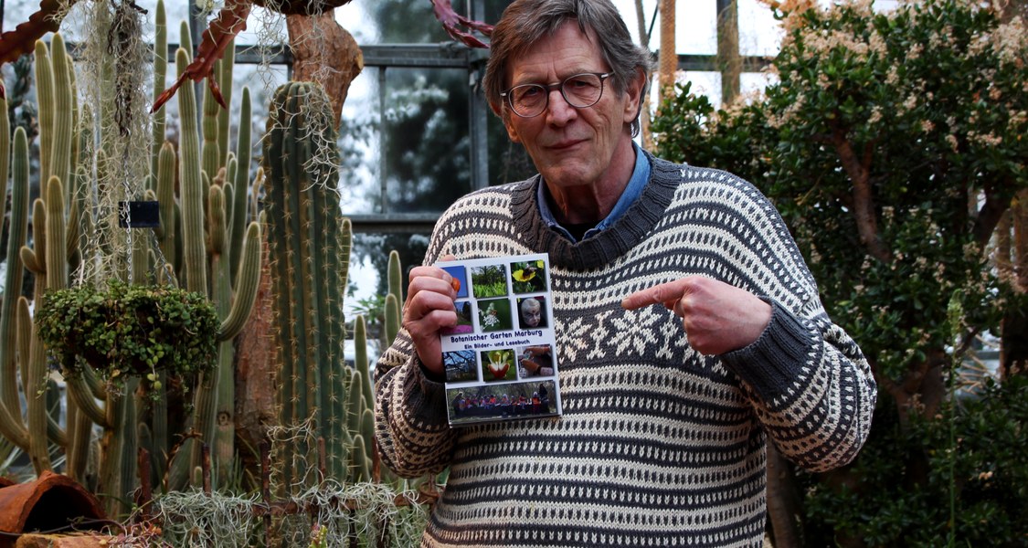 Das Foto zeigt Hartwig Bambey vom Sternbald Verlag mit seinem Werk "Botanischer Garten Marburg: Ein Bilder-Lese-Buch" im Botanischen Garten.