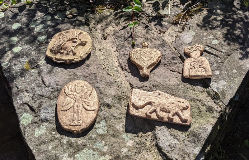 Mehrere fertigen Bronzereliefs liegen auf einem Steinwand, teilweise in Schatten