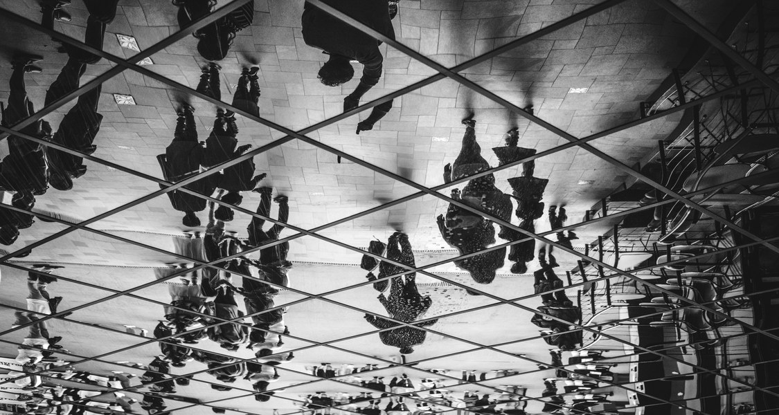 Abstraktes Foto in Schwarz-Weiß und mit starken Spiegelungen und Silhouetten von Menschen.