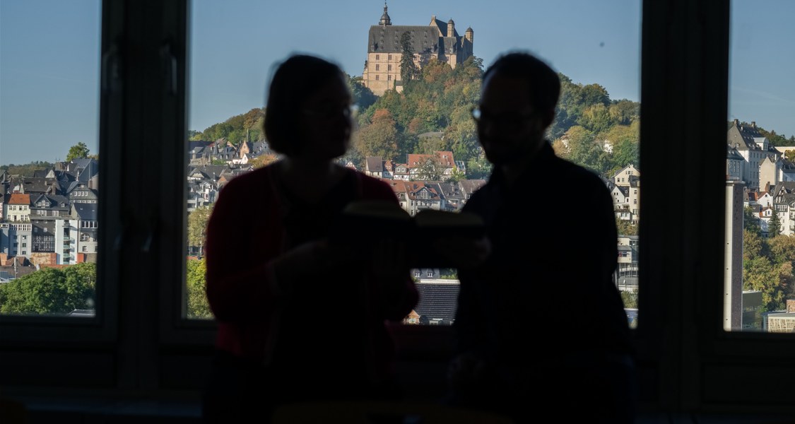 Zwei Forschende im Gespräch vor dem Hintergrund des Marburger Schlosses.