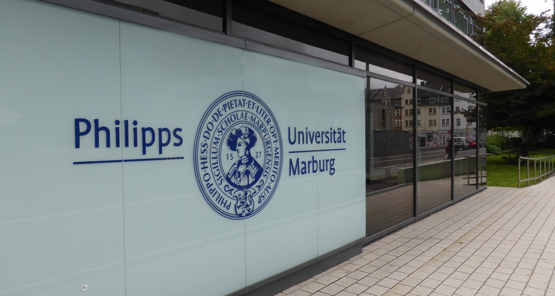 Eingang zu einem Gebäude. Auf der Wand des Gebäudes ist das Logo der Universität Marburg abgebildet.