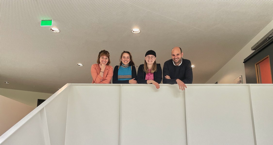 Vier Personen (Mitglieder der AG) schauen vom Treppengeländer nach unten