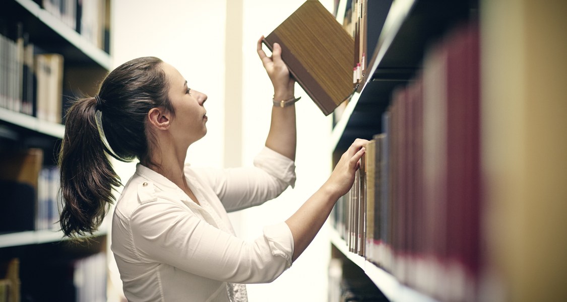 Studentin entnimmt Buch aus einem Regal in einer Bibliothek