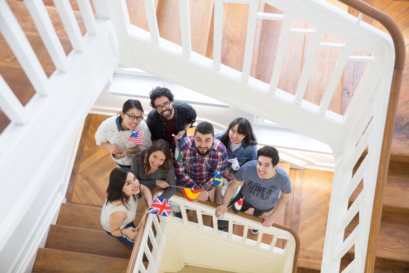 Austauschstudierende mit verschiedenen kleinen Landesflaggen im Treppenhaus des International Office in der Deutschhausstraße