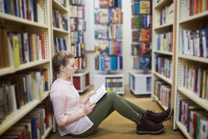 Eine Studierende liest ein Buch auf dem Boden einer Bibliothek