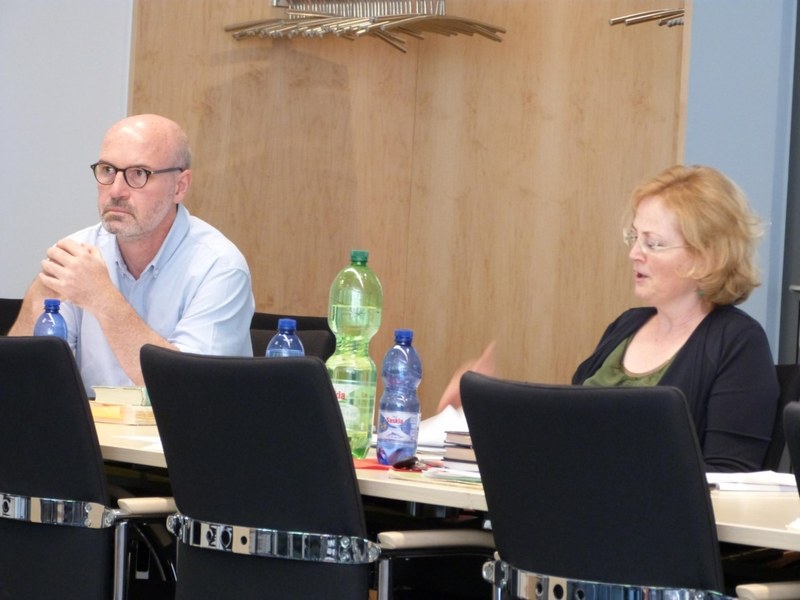 Blick über den Tisch auf Tagungsleiterin und Tagungsteilnehmer