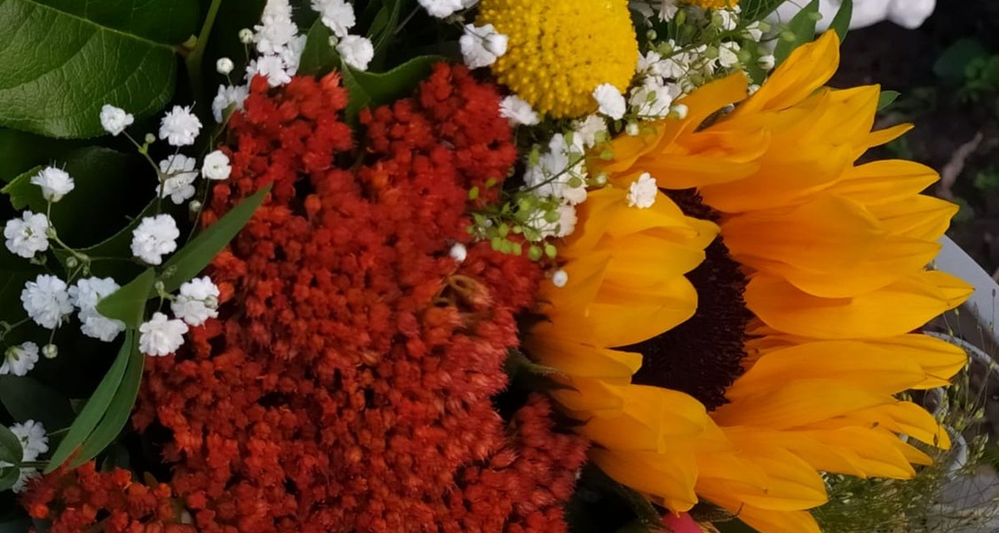 großer Blumenstrauß mit Sonnenblume in der Mitte und zwei Engeln links und rechts darüber, die auf den Strauß blicken