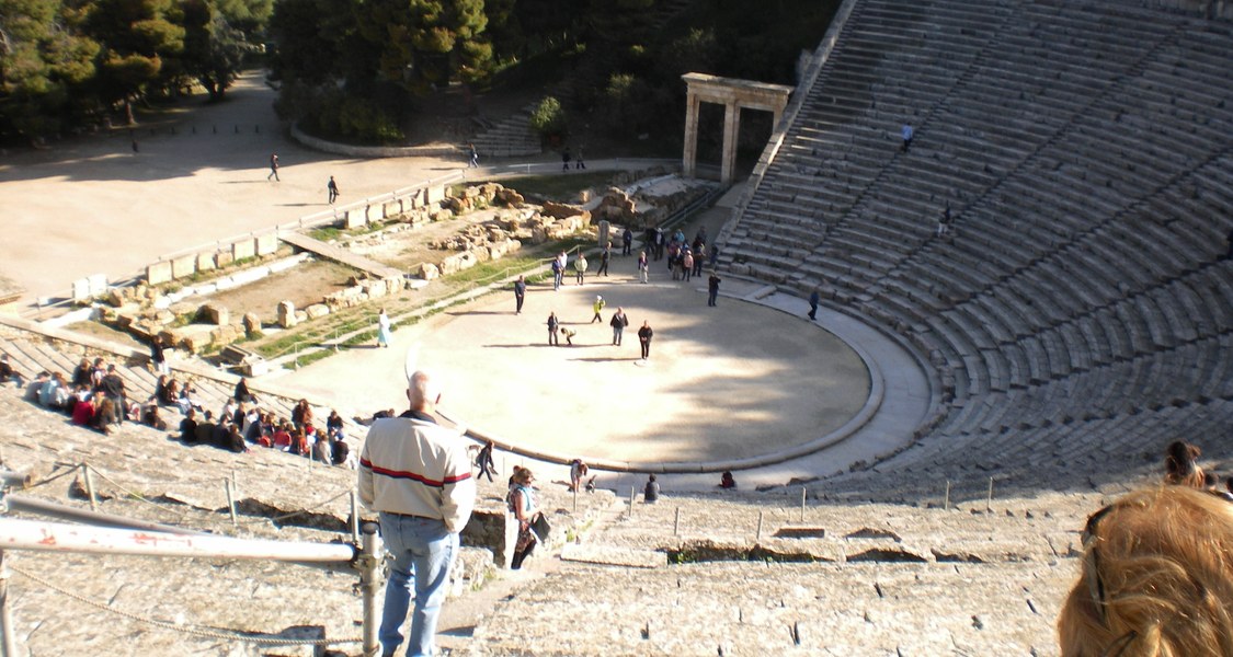 Blick von einer der oberen Sitzreihen in ein Amphitheater bei Sonnenschein