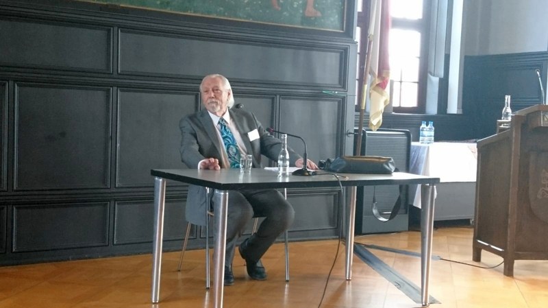 Henry Beissel sitzt an einem Tisch im historischen Rathaussaal von Marburg