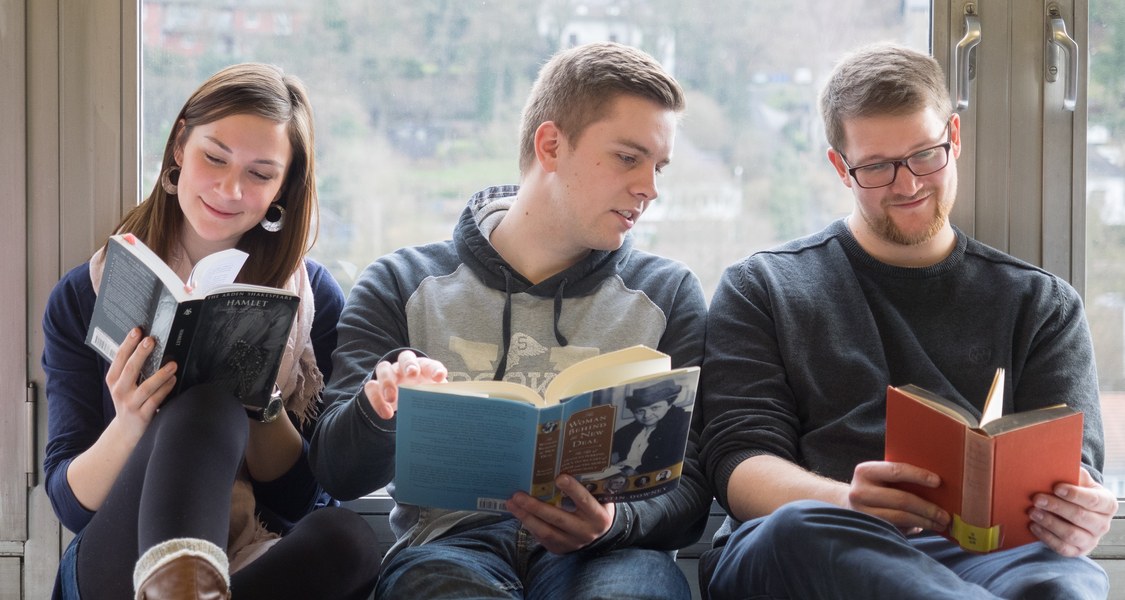 Studierende lesen Bücher vor einem Fenster der Philosophischen Fakultät