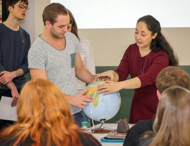 Professorin Agricola misst gemeinsam mit einem Studenten Distanzen auf ein Globus.