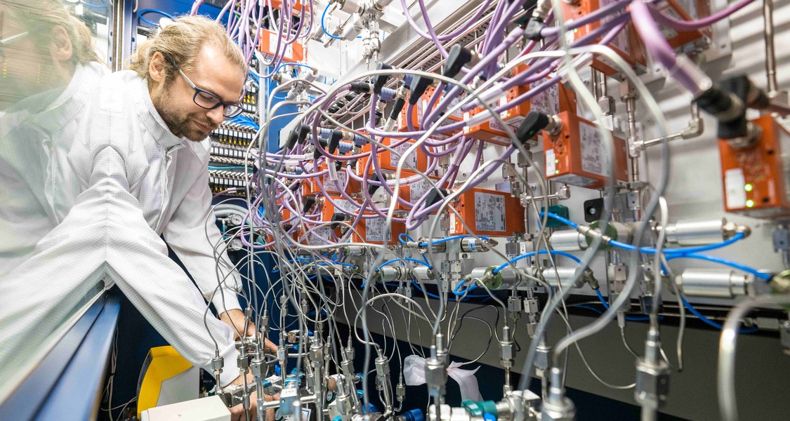 Ein Forscher greift in eine Präparationsapparatur mit ganz vielen Schläuchen und Ventilen