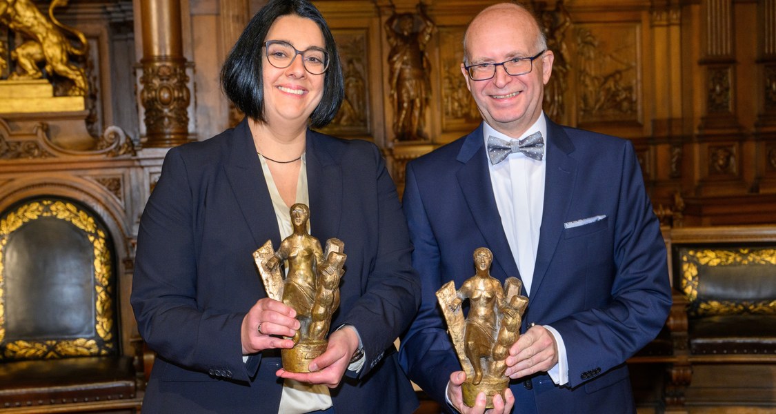 Die Preisträgerin und der Preisträger - beide halten eine kleine Skulptur in den Händen.