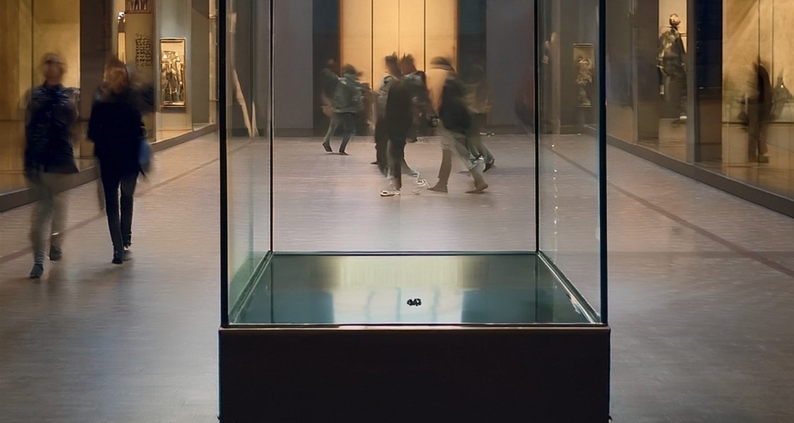 Eine leere Vitrine mit verschwommenen Besuchern im Hintergrund.